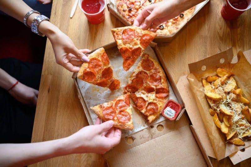 a group of people taking slices of pizza from a box