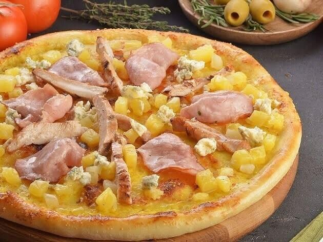 a pizza with meat and pineapple on a wooden board