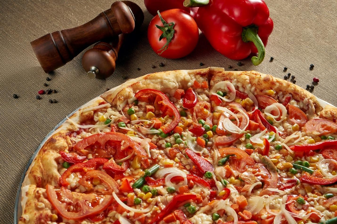 a pizza with vegetables and pepper shakers